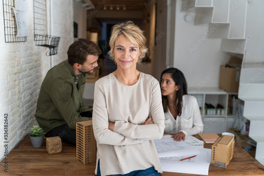 Portrait of confident mature woman in architectural office with colleagues in background Portrait of confident mature woman in architectural office with colleagues in background
