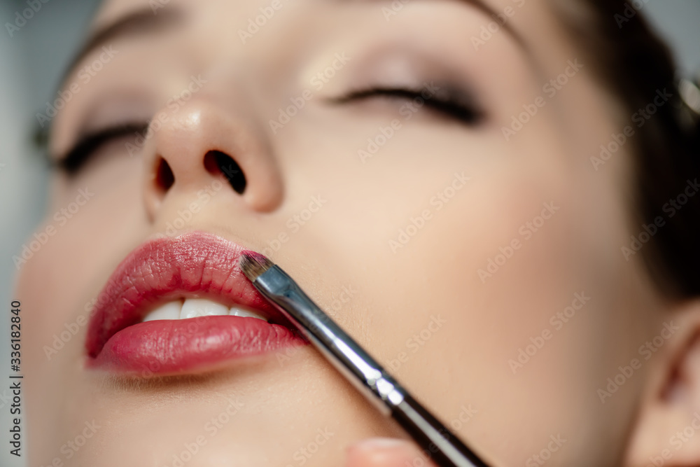 selective focus of cosmetic brush near lips of girl with closed eyes