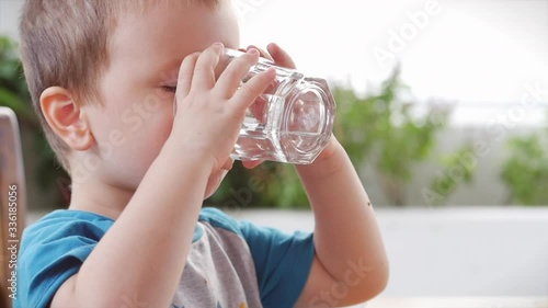 Cute baby boy drinking a glass of water in a cafe. Slow motion little boy drinking water. Close-up. The child is drinking a cup of water. photo