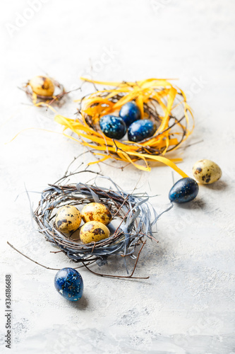 Easter Eggs in bird Nest. Quail easter eggs with feathers in nest on white table with copy space.