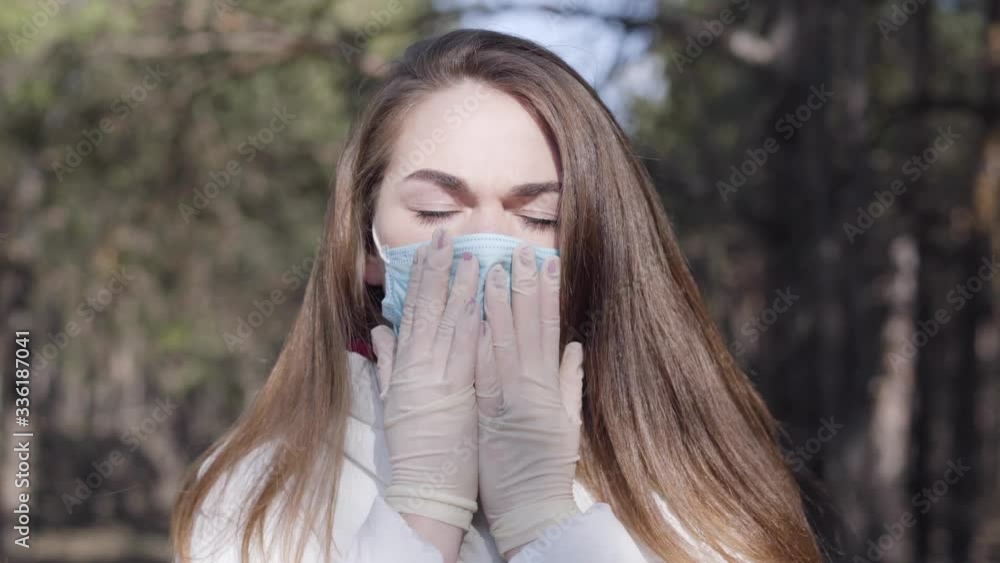 Close-up of young brunette woman in protective mask and gloves coughing in sunny spring park. Portrait of sick Caucasian girl having symptoms of coronavirus disease. Covid-19 pandemic, lifestyle. Close-up of young brunette woman in protective mask and gloves coughing in sunny spring park. Portrait of sick Caucasian girl having symptoms of coronavirus disease. Covid-19 pandemic, lifestyle.