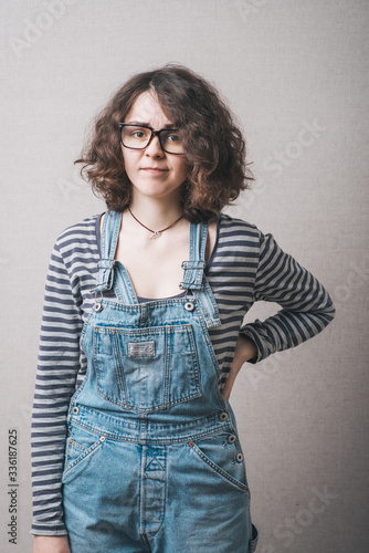 Woman in overalls dissatisfied stands with hand on hips. Gray background.