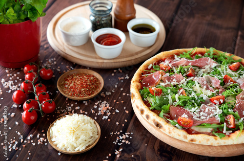 Italian pizza with arugula, cheese, ham. Top view. Pizza sauce, cherry tomatoes, salt, basil