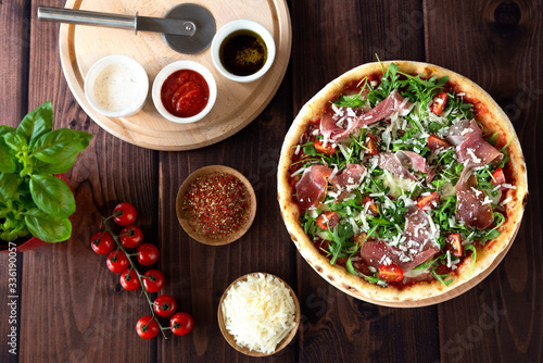Italian pizza with arugula, cheese, ham. Top view. Pizza sauce, cherry tomatoes, salt, basil