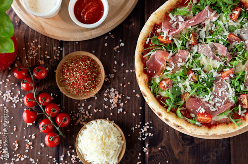 Italian pizza with arugula, cheese, ham. Top view. Pizza sauce, cherry tomatoes, salt, basil