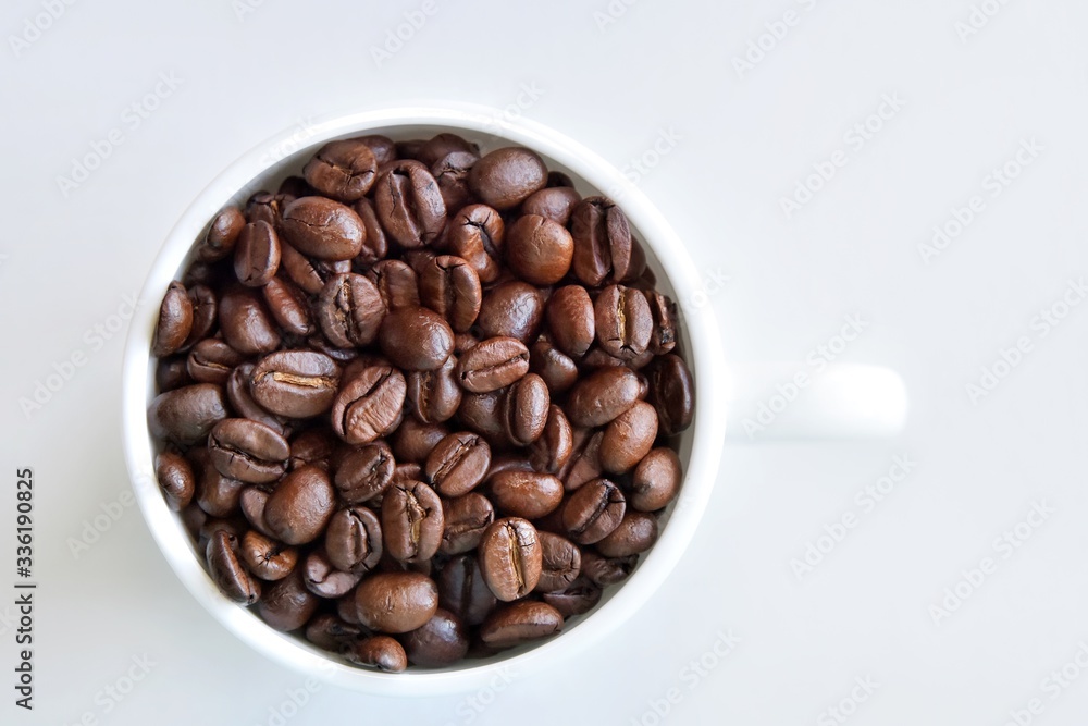 Roasted coffee beans in porcelain mug with selective focus on neutral background. Arabica coffee seeds in the coffee cup. Breakfast concept. Roasted coffee beans in porcelain mug with selective focus on neutral background. Arabica coffee seeds in the coffee cup. Breakfast concept.