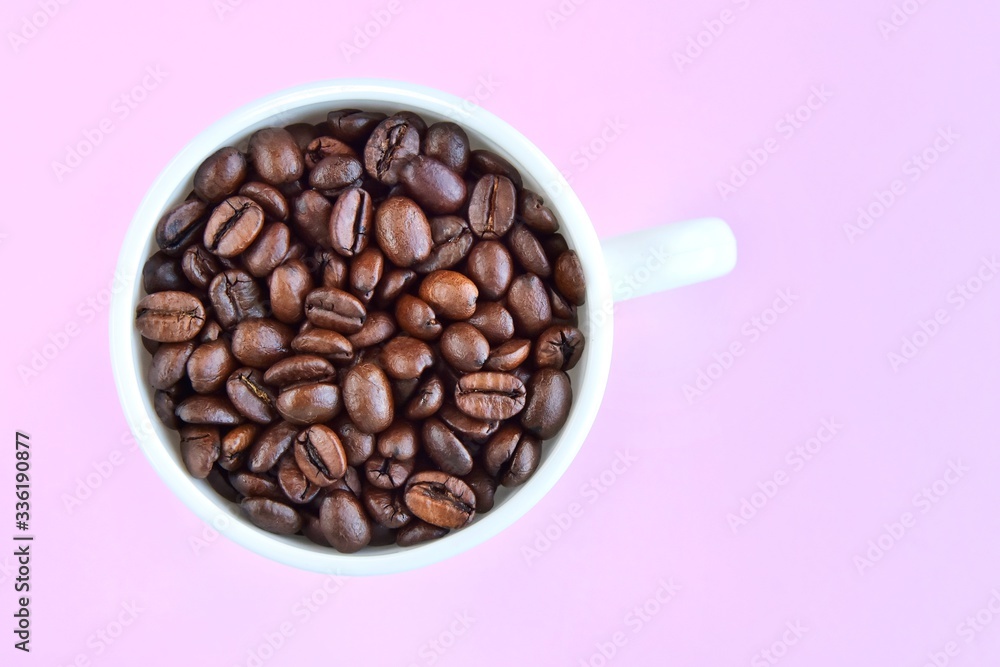 Roasted coffee beans in porcelain mug with selective focus on pink background. Arabica coffee seeds in the coffee cup. Breakfast concept. Roasted coffee beans in porcelain mug with selective focus on pink background. Arabica coffee seeds in the coffee cup. Breakfast concept.