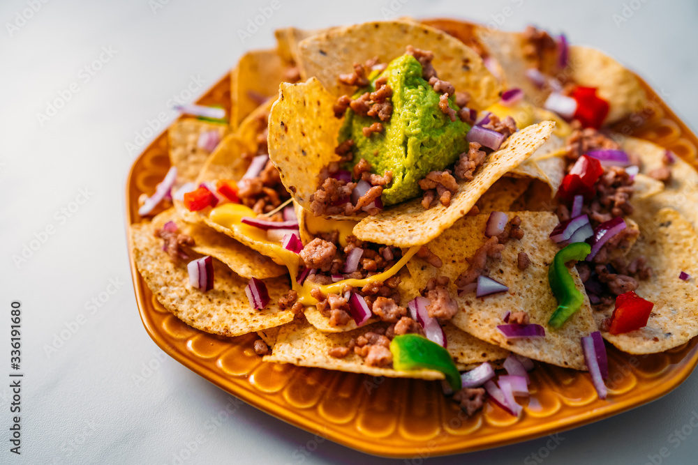 Close up of a plate of delicious Tortilla nachos corn chips with melted cheese sauce, ground beef, jalapeno peppers, red onion, salsa, and sour cream with guacamole dip. Top view Close up of a plate of delicious Tortilla nachos corn chips with melted cheese sauce, ground beef, jalapeno peppers, red onion, salsa, and sour cream with guacamole dip. Top view