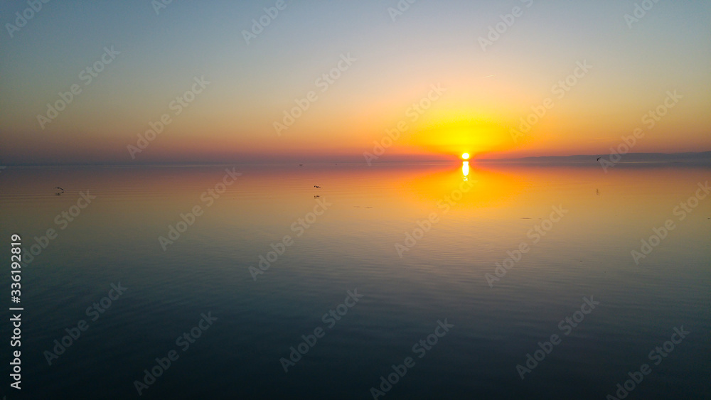 Sundown with straight horizon line, colourful sky and calm smooth water. Sunset, beautiful panorama view from a lake beach

