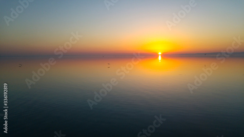 Sundown with straight horizon line, colourful sky and calm smooth water. Sunset, beautiful panorama view from a lake beach 