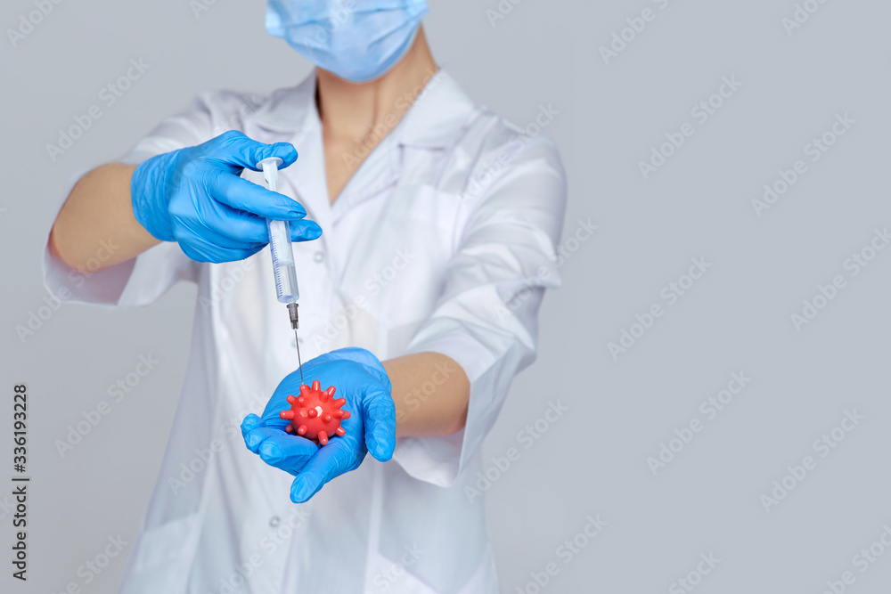 woman doctor in white uniform, mask and rubber gloves holding syringe and virus model on gray background. pandemic treatment. focus on hand. copy space woman doctor in white uniform, mask and rubber gloves holding syringe and virus model on gray background. pandemic treatment. focus on hand. copy space
