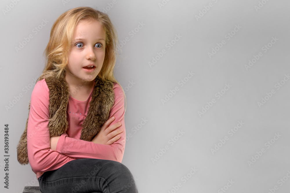 portrait of surprised blond child girl of 8 years old, portrait of emotional little kid in pink T-shirt and fur vest in studio on the grey background, copy space portrait of surprised blond child girl of 8 years old, portrait of emotional little kid in pink T-shirt and fur vest in studio on the grey background, copy space