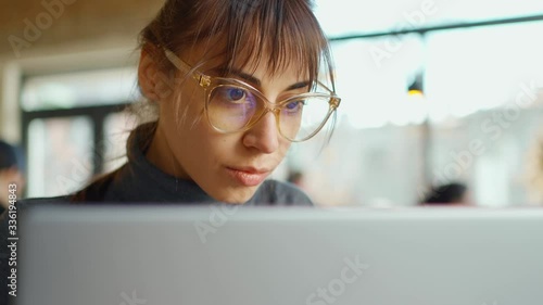 closeup face of Young business woman in eyeglasses concentrating on screen and typing on laptop while sitting at workplace or cafe. remote work, freelance, using laptop