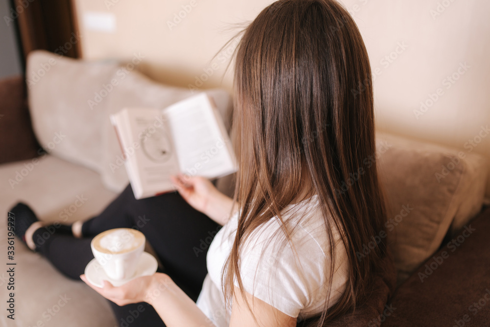Young attractive woman read the book at home. Quarantine time. Woman drink cappuchino and fill the notebook