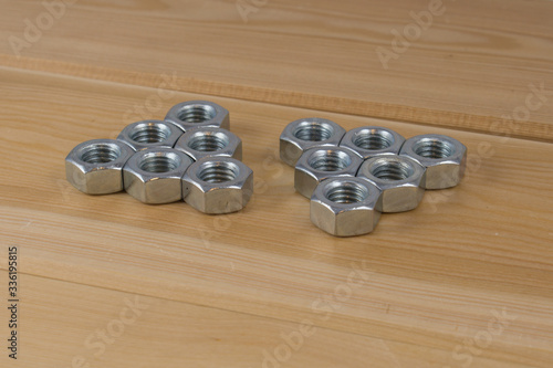Dziesięć metalowych nakrętek, ułożone w dwóch grupach na drewnianej desce