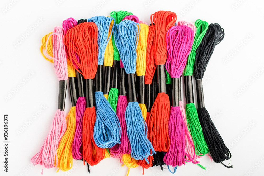 Fototapeta premium Many mixed vivid colored sewing threads for embroidery isolated on a white table, top view or flat lay of red, pink, yellow, blue, black and green textile materials