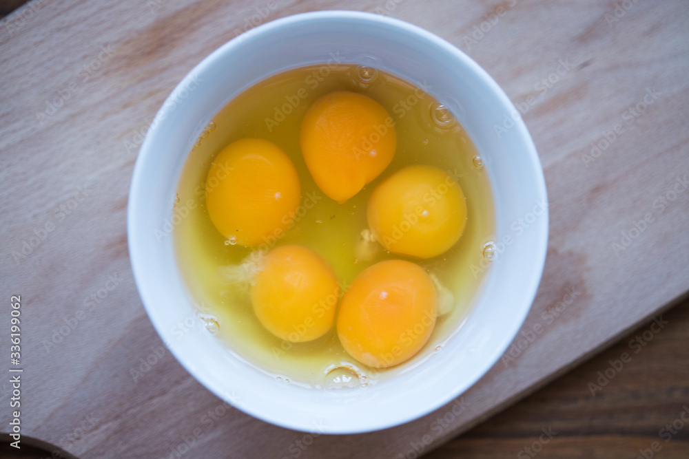 Picture of raw, broken eggs in a white bowl, top view Picture of raw, broken eggs in a white bowl, top view