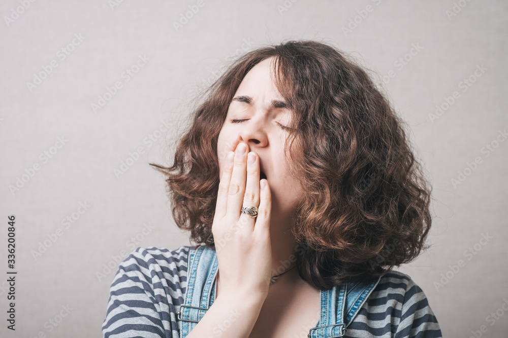 The woman yawns. On a gray background. The woman yawns. On a gray background.