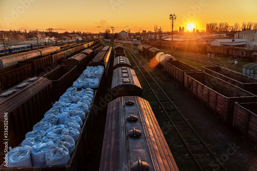 Train wagons carrying cargo containers for shipping companies. Distribution and freight transportation using railroads. Station during a warm sunset. White industrial bags are in the wagon.