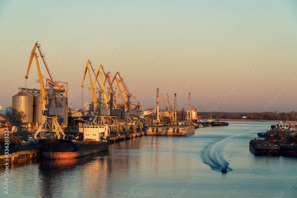 View of the shipyard at the sunset with historical cranes and ships in the industrial part of the city. Port with many containers and tug boats.