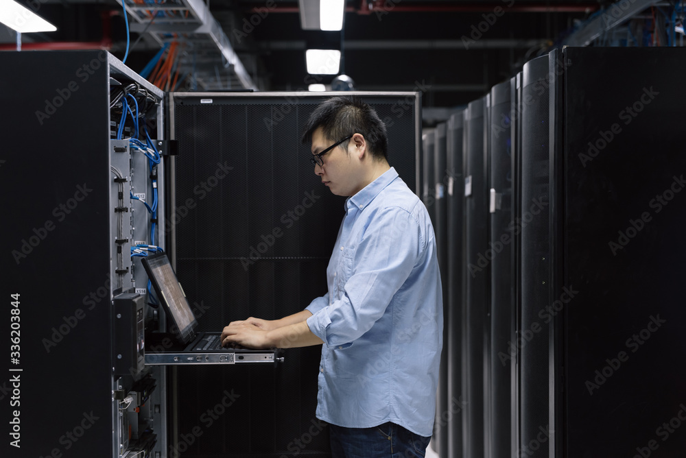Server room technician using computer in server room Server room technician using computer in server room