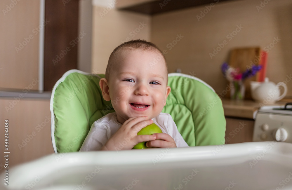 Baby boy sits in a chair and eats green apple Baby boy sits in a chair and eats green apple