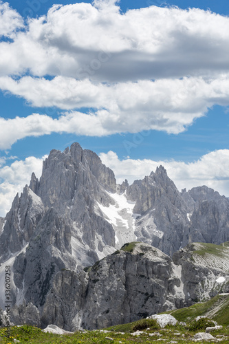 Iconic Italian mountainscape with a green meadow in the foreground and distant rocky peaks in the background, under a blue sky with puffy clouds