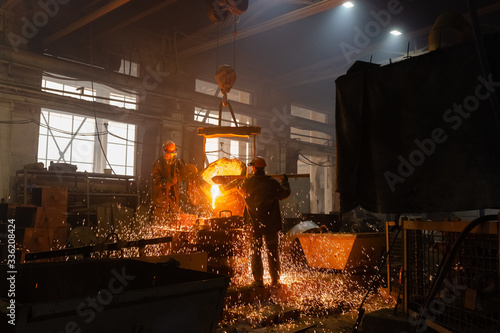 Men pouring sparkling metal in mold in foundry