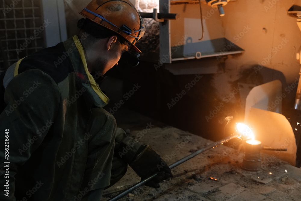 Foundry worker pouring hot metal in mold Foundry worker pouring hot metal in mold