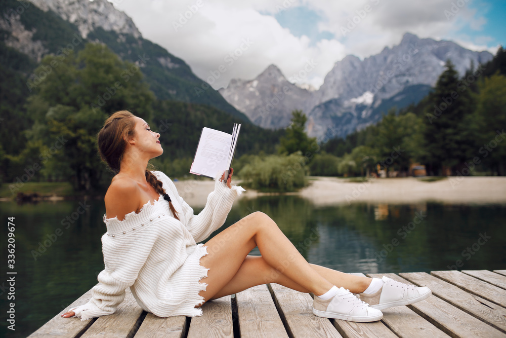 Attractive young woman reading book on dock next to the lake