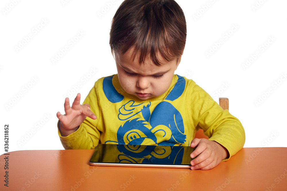 Young child girl is using tablet while sitting at table, isolated over white background Young child girl is using tablet while sitting at table, isolated over white background