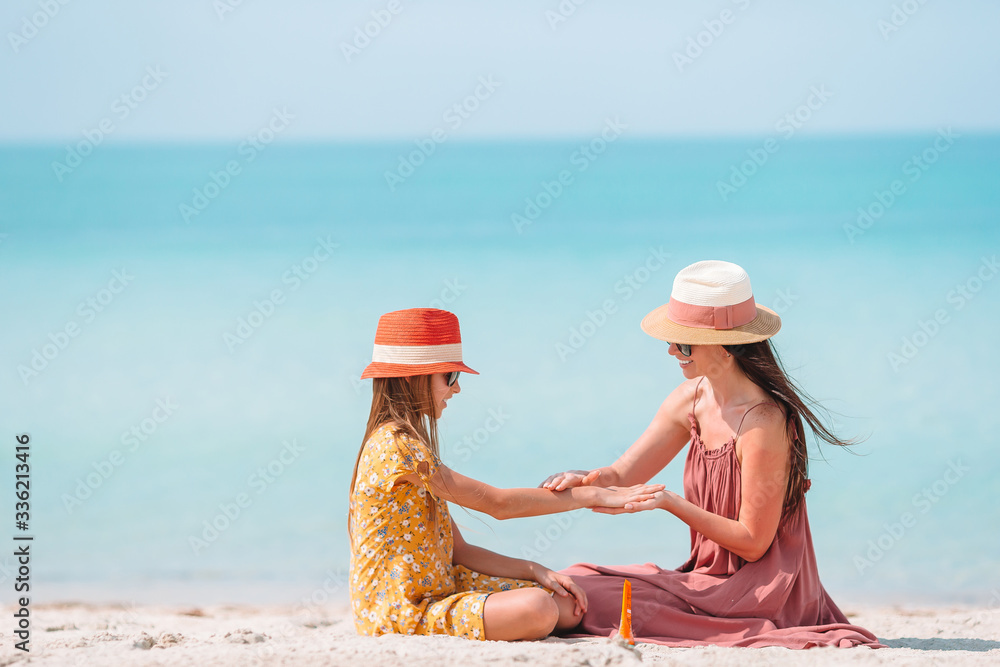 Young mother applying sun cream to daughter nose on the beach. Sun protection