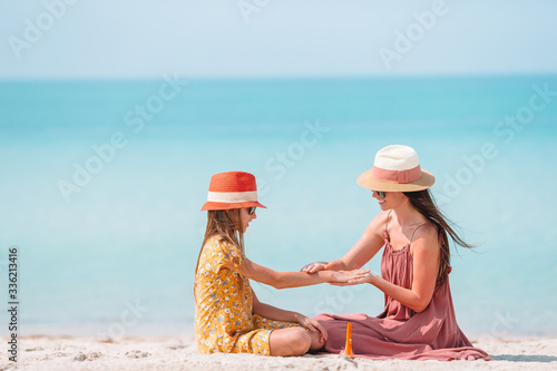 Obraz na płótnie Young mother applying sun cream to daughter nose on the beach. Sun protection w salonie