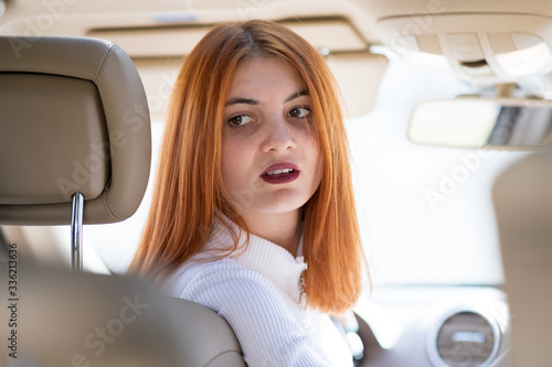 Young redhead woman driver driving a car backwards.