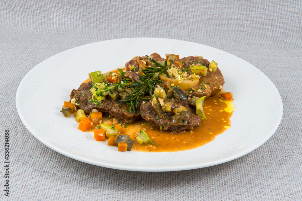 Large stews of beef meat with vegetables in a large white plate on a gray background Large stews of beef meat with vegetables in a large white plate on a gray background