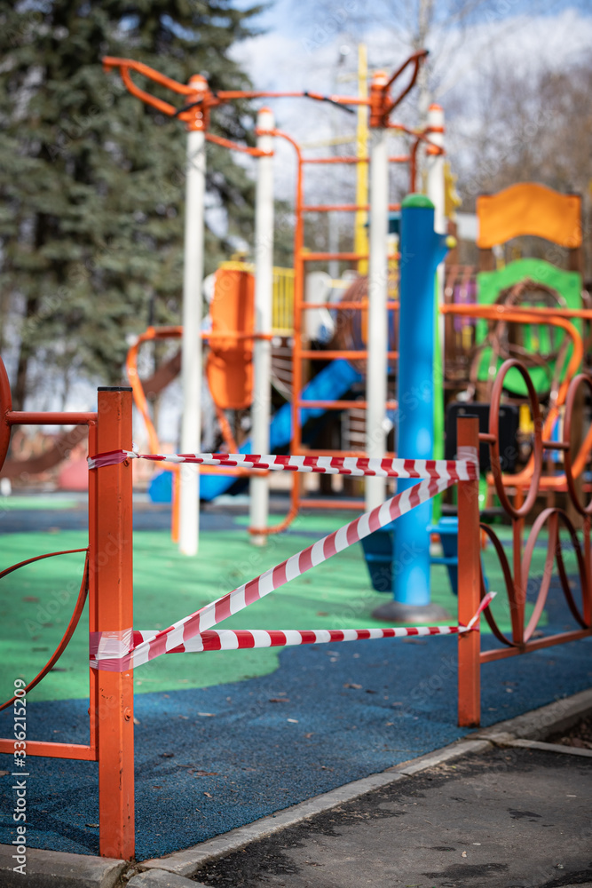 Fototapeta premium Covid-19 coronovirus infection pandemic. Fenced playground. The entrance is wound with warning tape in white and red. Everyone is sitting at home. Empty area without children.