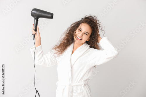 Beautiful young African-American woman with blow dryer on light background