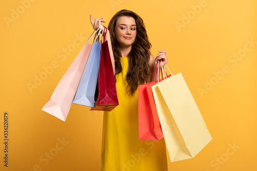 beautiful smiling girl in spring dress holding shopping bags on yellow