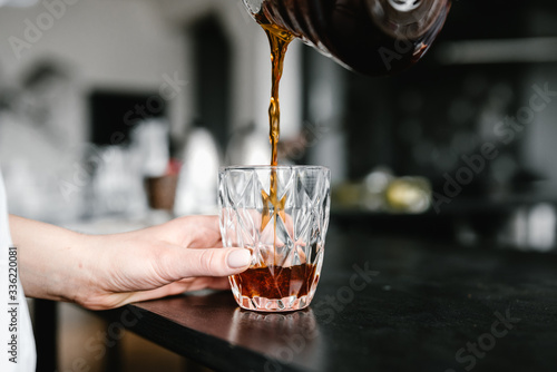 Barista pouring black coffee in glass.