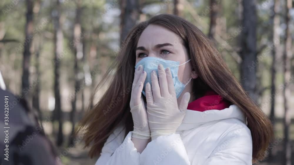 Portrait of young Caucasian woman in face mask talking to unrecognizable man and coughing. Brunette lady with coronavirus symptoms chatting with boy outdoors. Covid-19 pandemic risk. Portrait of young Caucasian woman in face mask talking to unrecognizable man and coughing. Brunette lady with coronavirus symptoms chatting with boy outdoors. Covid-19 pandemic risk.