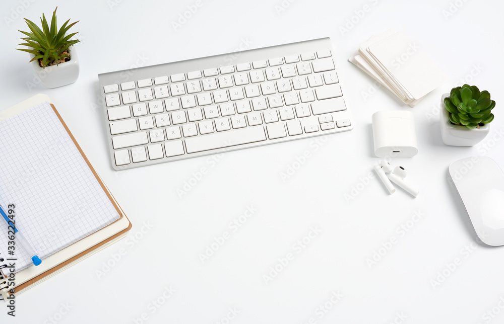 White wireless keyboard, a stack of notebooks, green plants in pots and a mouse, workplace of a freelancer White wireless keyboard, a stack of notebooks, green plants in pots and a mouse, workplace of a freelancer
