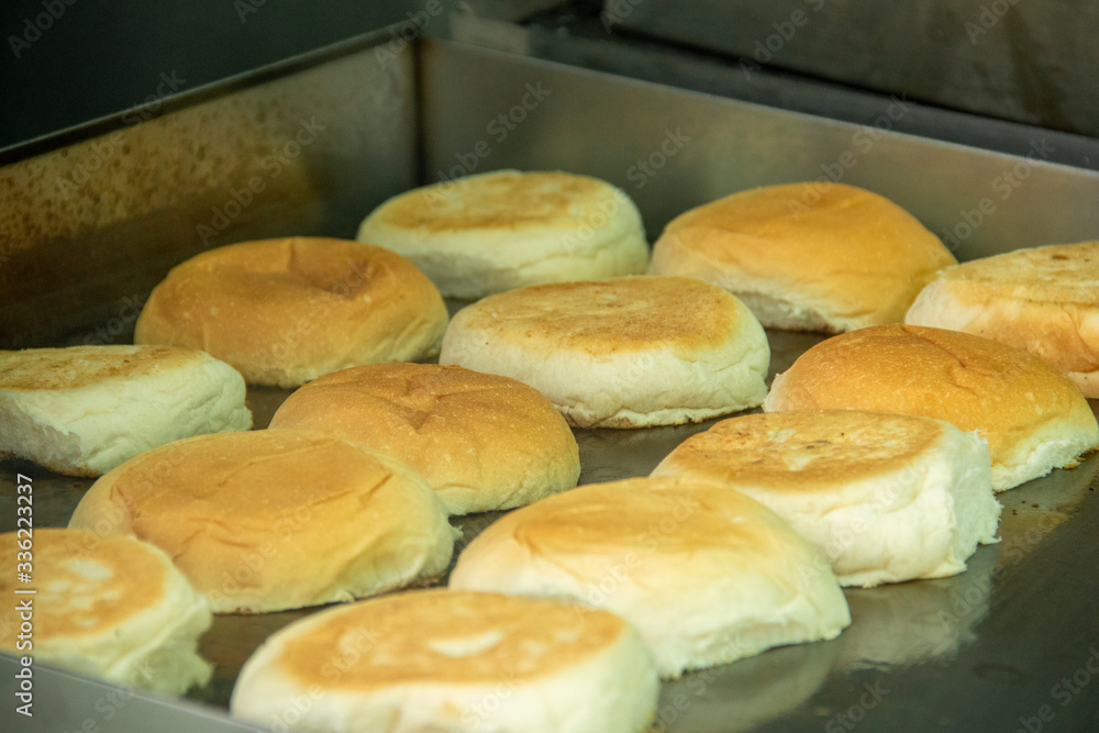 Group of sliced hamburger buns being toasted on a griddle