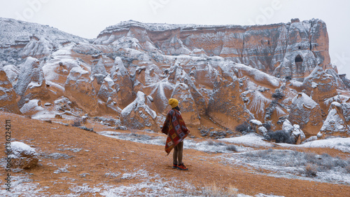 Woman alone with the volcanic landscape at Devrent Valley in Cappadocia. Girl walking around Fairy chimneys surronded by tufa formations at Imaginary Valley in winter season in Cappadocia, Turkey.