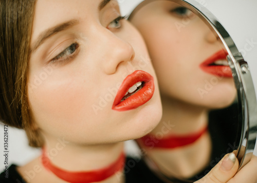 The portrait of a girl with red weird lipstick and the mirror in her hands and her reflection there. photo