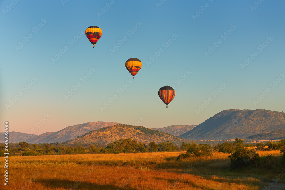 Hot air balloons with tourists above the Pilanesberg reserve. Three hot air balloons, decorated safari motifs against blue sky, mountains on background. Holiday Safari in South Africa.