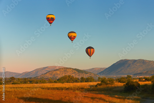 Hot air balloons with tourists above the Pilanesberg reserve. Three hot air balloons, decorated safari motifs against blue sky, mountains on background. Holiday Safari in South Africa. photo
