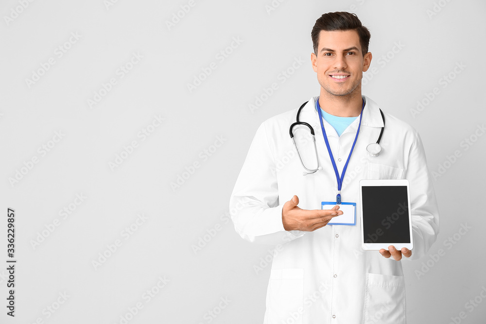 Portrait of young male doctor with tablet computer on light background