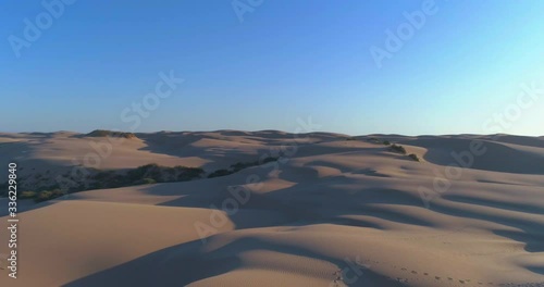Beautiful 4k aerial video of sand dunes fly over with people walking at sunset