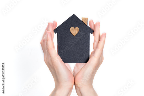 Female hands surround a model of a dark house on a light background. Real estate and insurance concept. Protecting your family at your fingertips