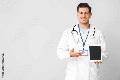 Portrait of young male doctor with tablet computer on light background